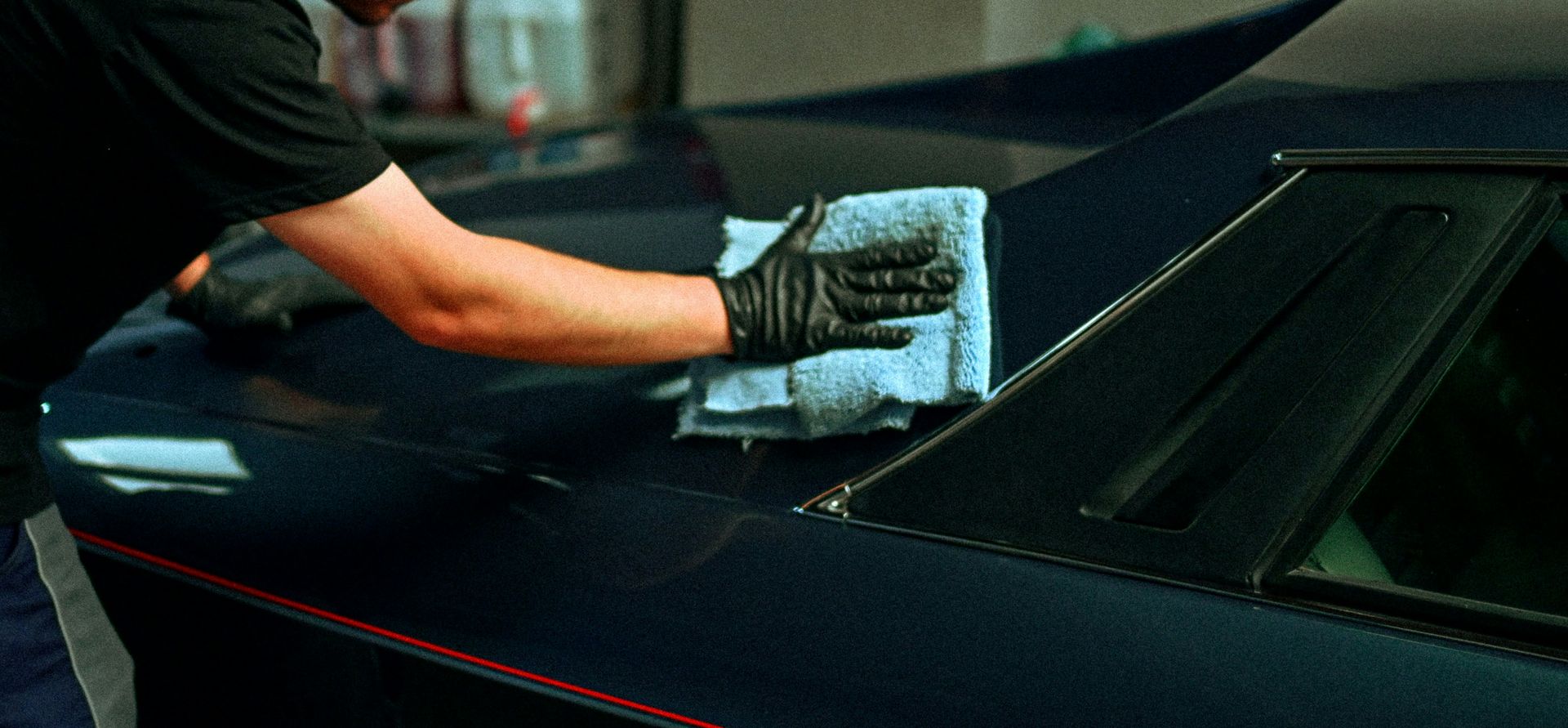 A person polishing a dark blue car with a cloth.